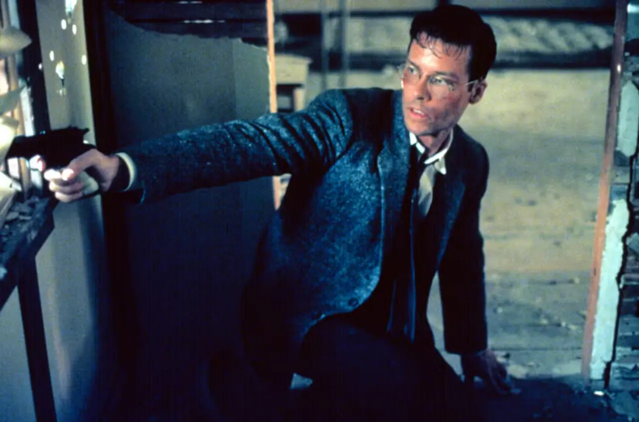 Guy Pearce, sweaty and bloodied, points a pistol off-screen in L.A. Confidential