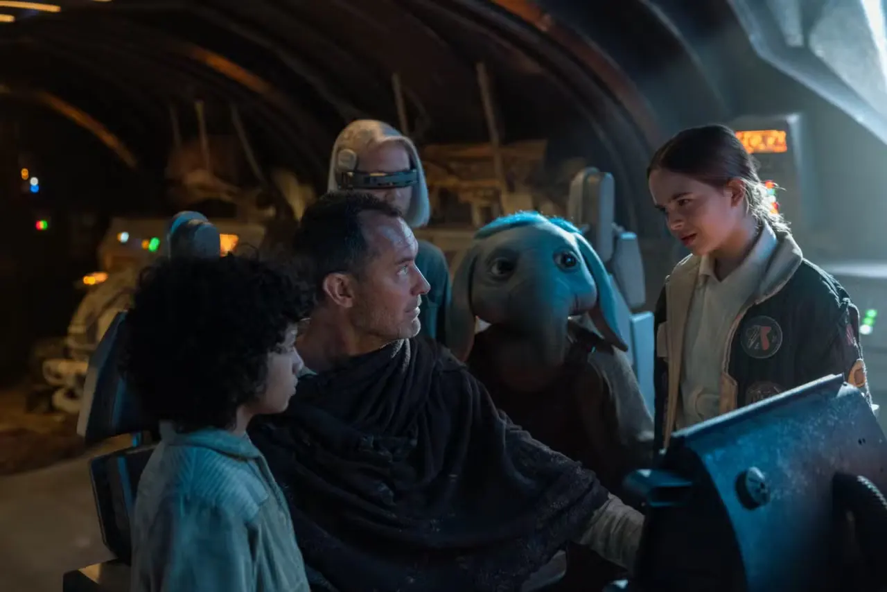 Jude Law Jedi huddles with some kids including a kid Ortolan aka Baby Max Rebo in a spaceship cockpit in Star Wars: Skeleton Crew