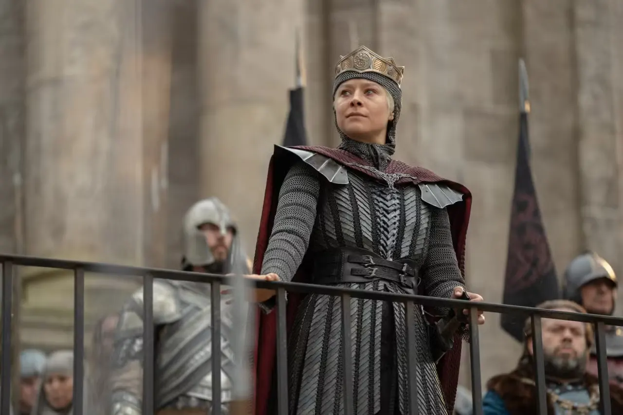 Queen Rhaenyra Targaryen (Emma D'Arcy) looks over a railing while her guards and council stand behind her in House of the Dragon
