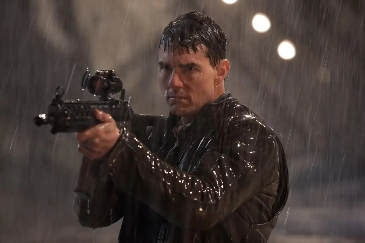 Tom Cruise stands in the rain holding a big gun