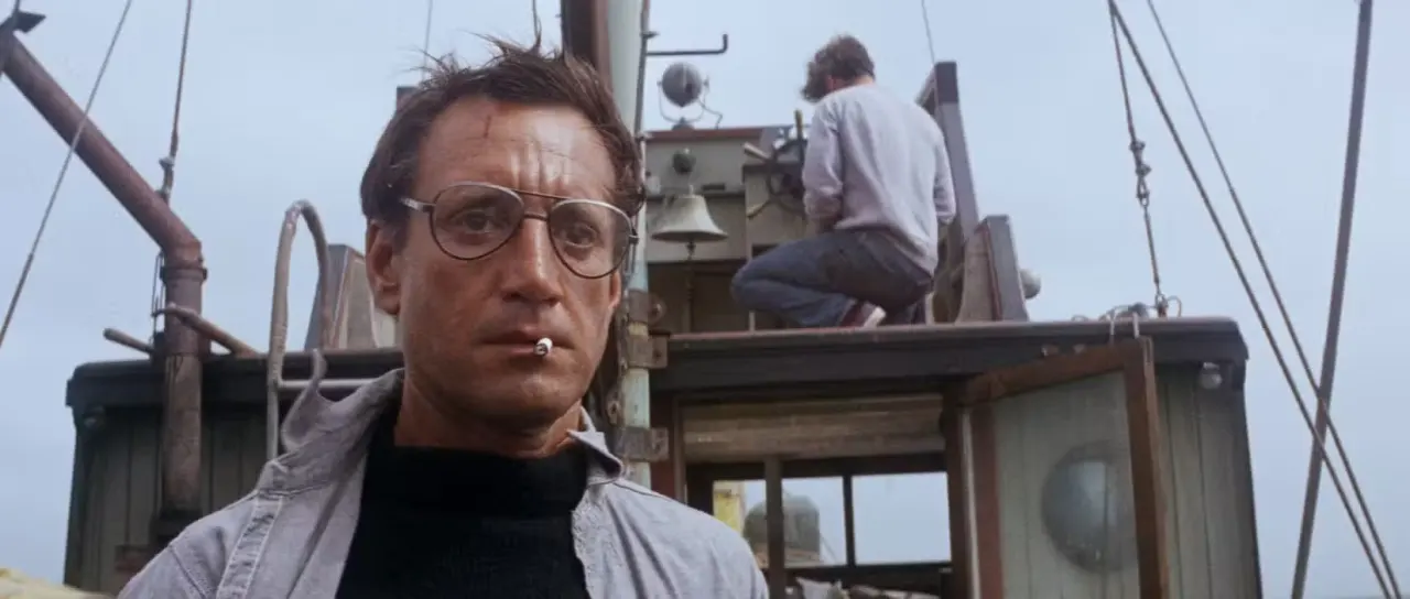 Roy Scheider as Hooper wearing big glasses and smoking a cigarette, stares in shock at the backend of a boat in Jaws